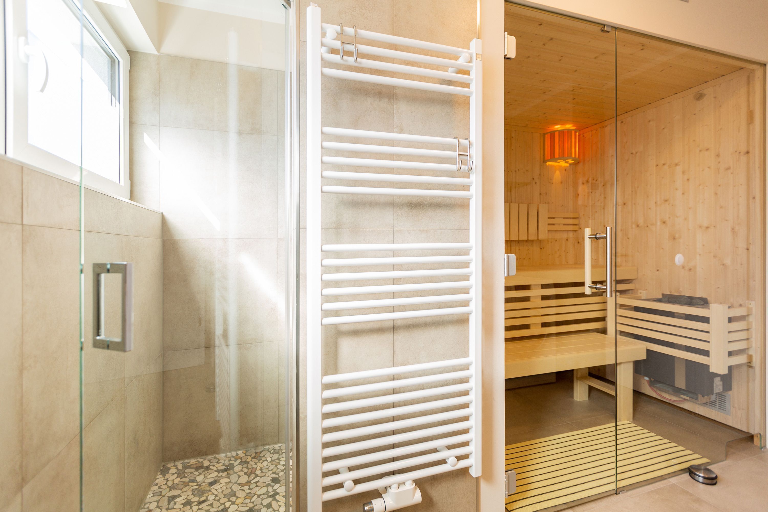 A modern bathroom with a glass shower enclosure, a white towel rack, and a wooden sauna area.