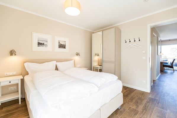 A bedroom with a bed, bedside tables, a nightstand, a mirror, and a door leading to another room.
