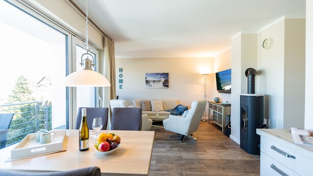 A modern living room with a dining area, a sofa set, a TV, a kitchen area, and a large window. - Quartier am Fischerstrand, App. 3 (Heringsdorf)