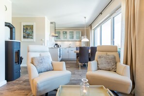 A modern living room with two sofas, a coffee table, a fireplace, and a kitchen in the background. - Quartier am Fischerstrand, App. 3 (Heringsdorf)