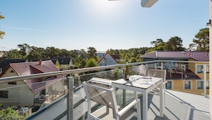 Ein Balkon mit Glasgeländer, einem Tisch und einer Flasche.