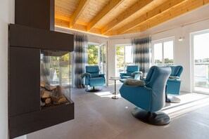 Una sala de estar moderna con sofás azules, una chimenea de vidrio y grandes ventanales con vistas al exterior.