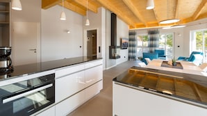Eine moderne Küche mit weißen Schränken, einer schwarzen Arbeitsplatte und einem eingebauten Ofen. Ein Essbereich mit Tisch und Stühlen lädt zum Verweilen ein, und ein großes Fenster sorgt für natürliches Licht.