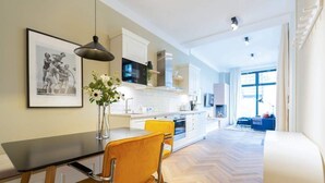 A modern kitchen with white cabinets, a black microwave, and a dining area with a wooden table and yellow chairs. - Villa Bellevue, App. 03 (Heringsdorf)