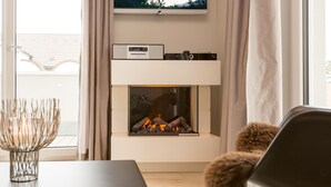 A modern living room with a fireplace, a flat-screen TV mounted above it, and a dining area with a table and chairs. - Dune Residence Heringsdorf, App. 22 (Heringsdorf)