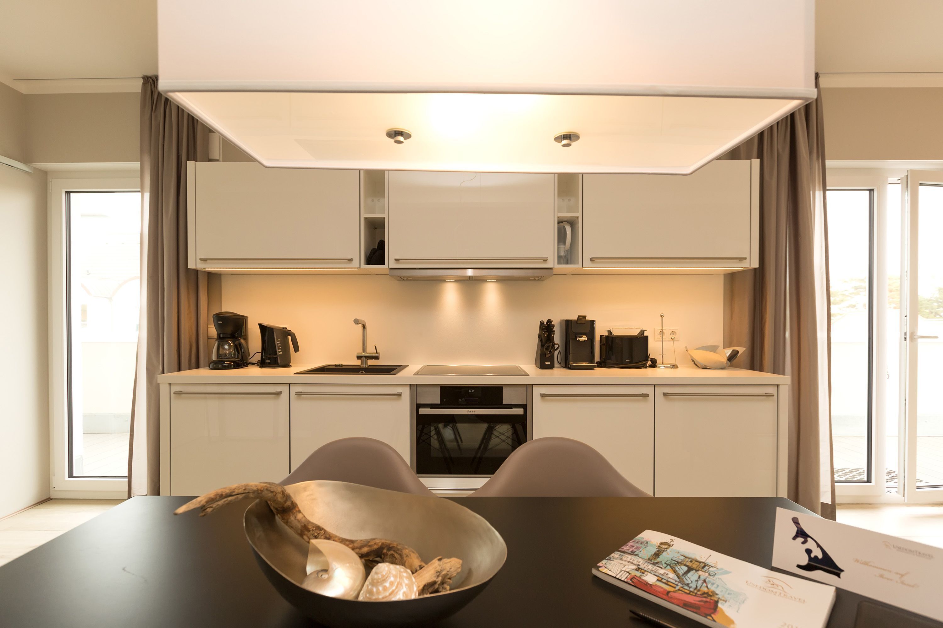 A modern kitchen with built-in appliances, a dining table with chairs, and a large window.