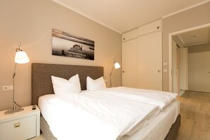 Et hotelværelse med en stor seng, to sengeborde, lamper, et billed på væggen og et klædeskab.