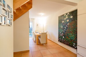 A dining area with a wooden table and chairs, a large floral painting on the wall, and a view of the outdoors through a door. - Silva Vacation Cottage, Germany (Koserow)