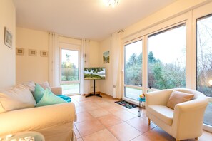 A living room with two sofas, a TV, and large windows with a view of trees. - Silva Vacation Cottage, Germany (Koserow)