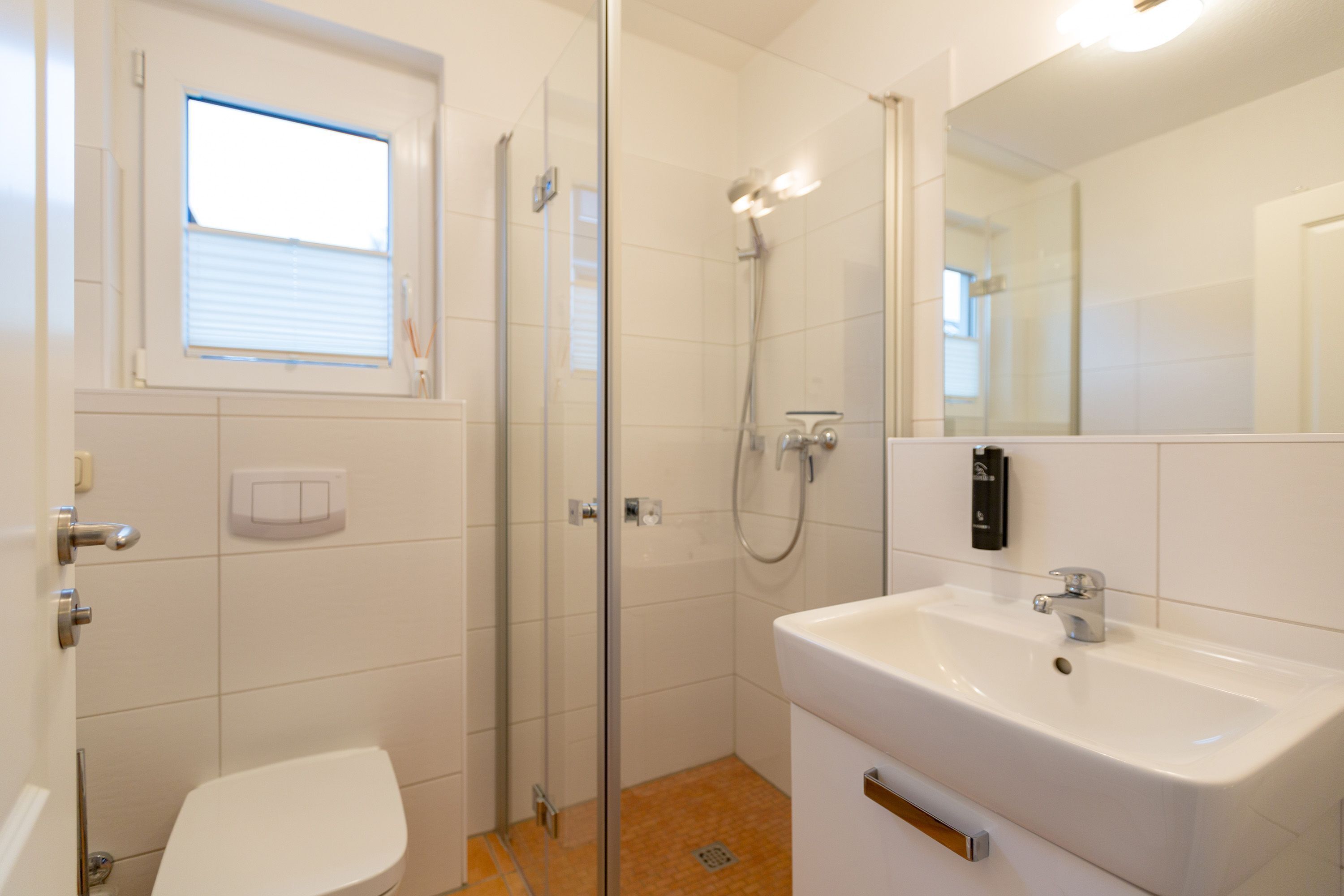 A bathroom with a toilet, a sink, a shower, and a window.