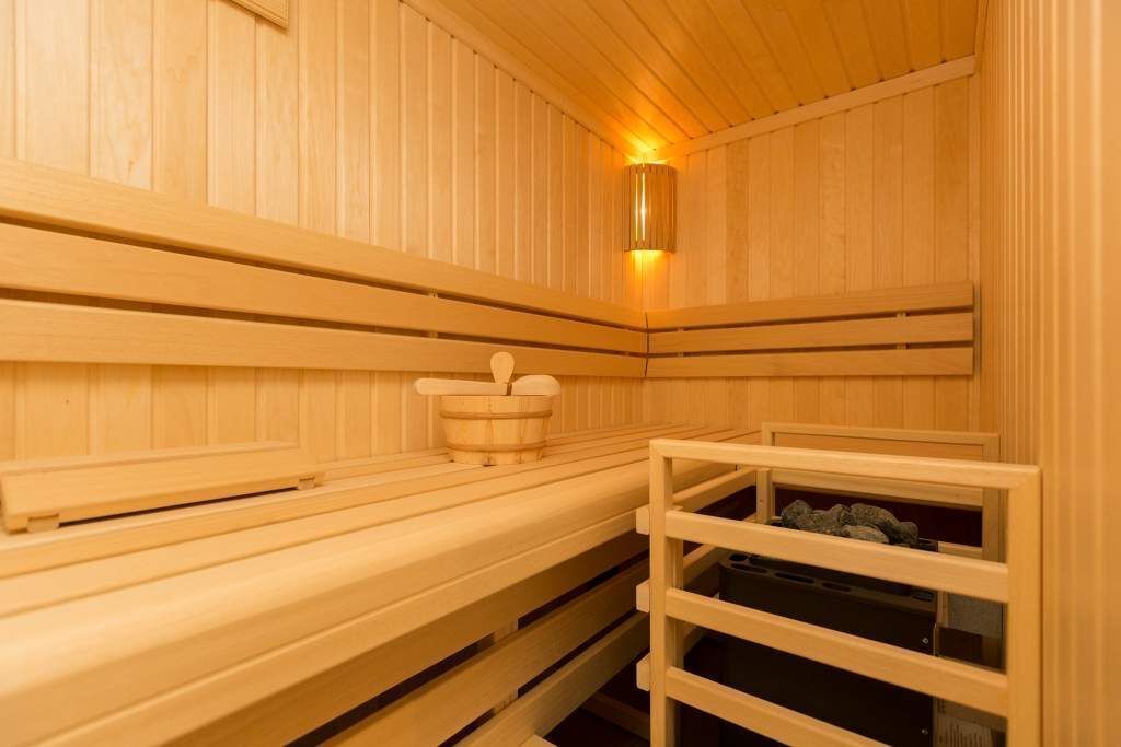 Uma sauna de madeira com bancos, um aquecedor fixado na parede e uma prateleira com pedras.