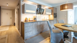 A modern kitchen with wooden cabinets, a built-in oven, and a dining area with a round table and chairs. - Dune Residence Heringsdorf, App. 17 (Heringsdorf)