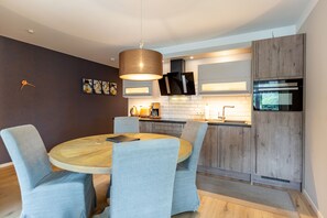 Une cuisine moderne avec une table ronde en bois et des chaises à revêtement gris, un four encastré et un luminaire suspendu.