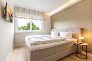 Une chambre à coucher avec un lit, une table de chevet avec une lampe, une fenêtre avec des rideaux et un téléviseur fixé au mur.