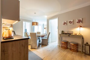 A modern kitchen with a wooden countertop, a kettle, and a dining area with chairs and a table.