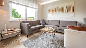 A modern living room with a grey sofa, a glass coffee table, and a large abstract painting on the wall. - Dune Residence Heringsdorf, App. 17 (Heringsdorf)