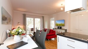 A modern kitchen with white cabinets, a black countertop, and a dining area with a white table and chairs. - Dune Residence Heringsdorf, App. 18 (Heringsdorf)