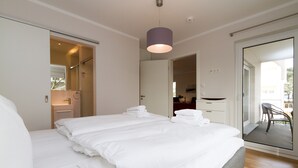 A modern hotel room with a large bed, a bathroom with a shower, and a balcony with a chair. - Dune Residence Heringsdorf, App. 18 (Heringsdorf)