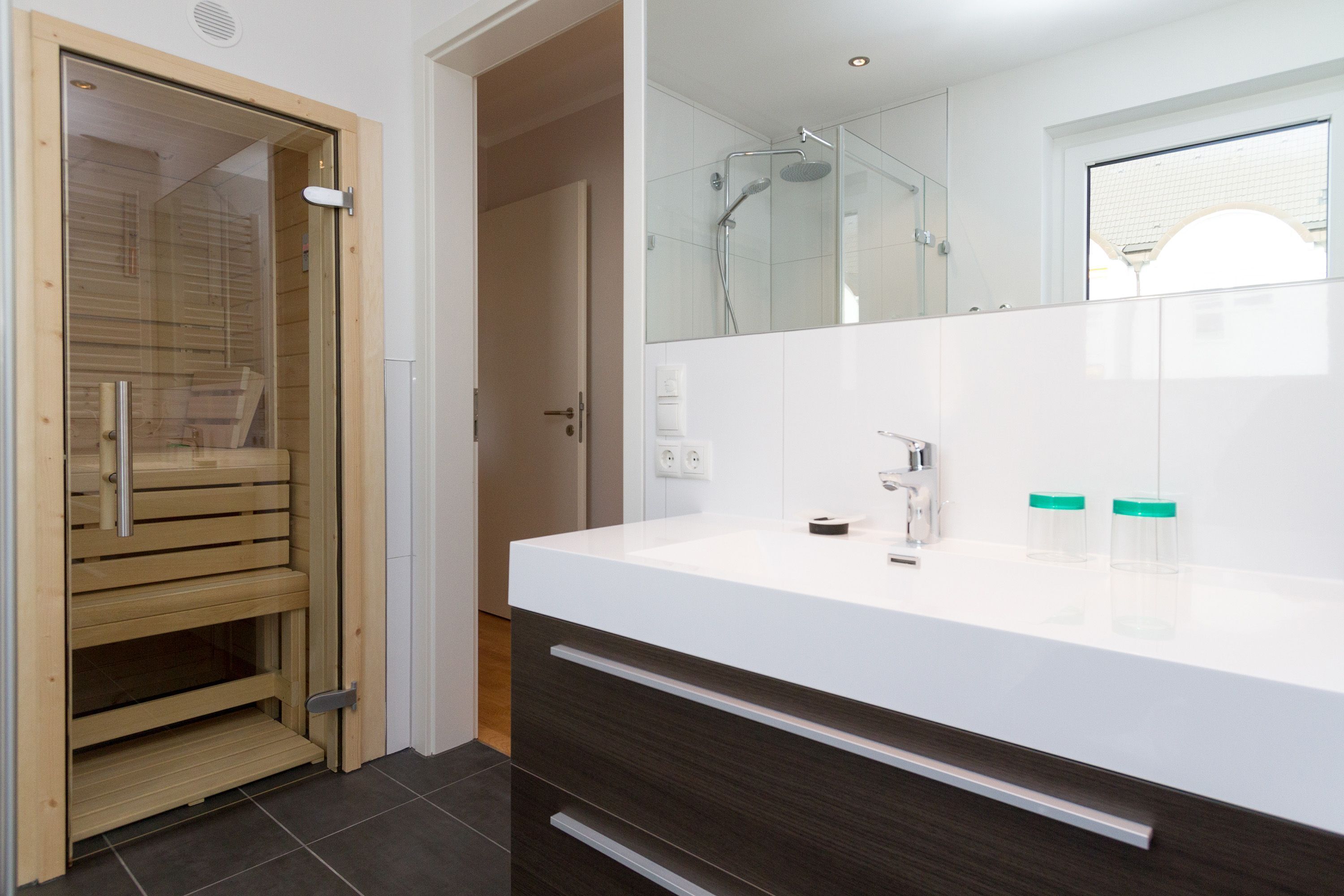 A modern bathroom with a wooden sauna door, a white sink, and a large mirror.