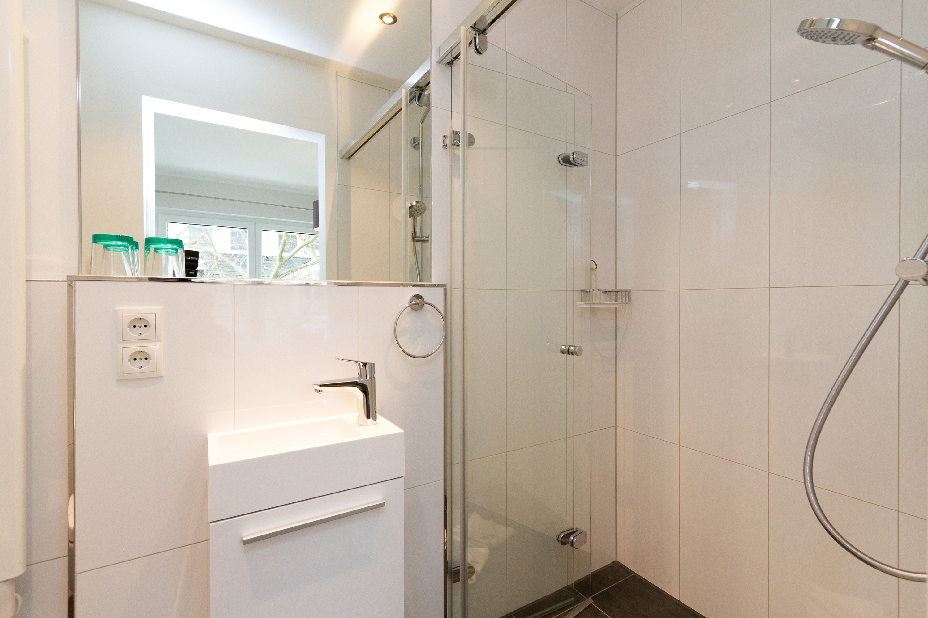 Un baño moderno con ducha de vidrio, un lavabo blanco y un espejo encima.