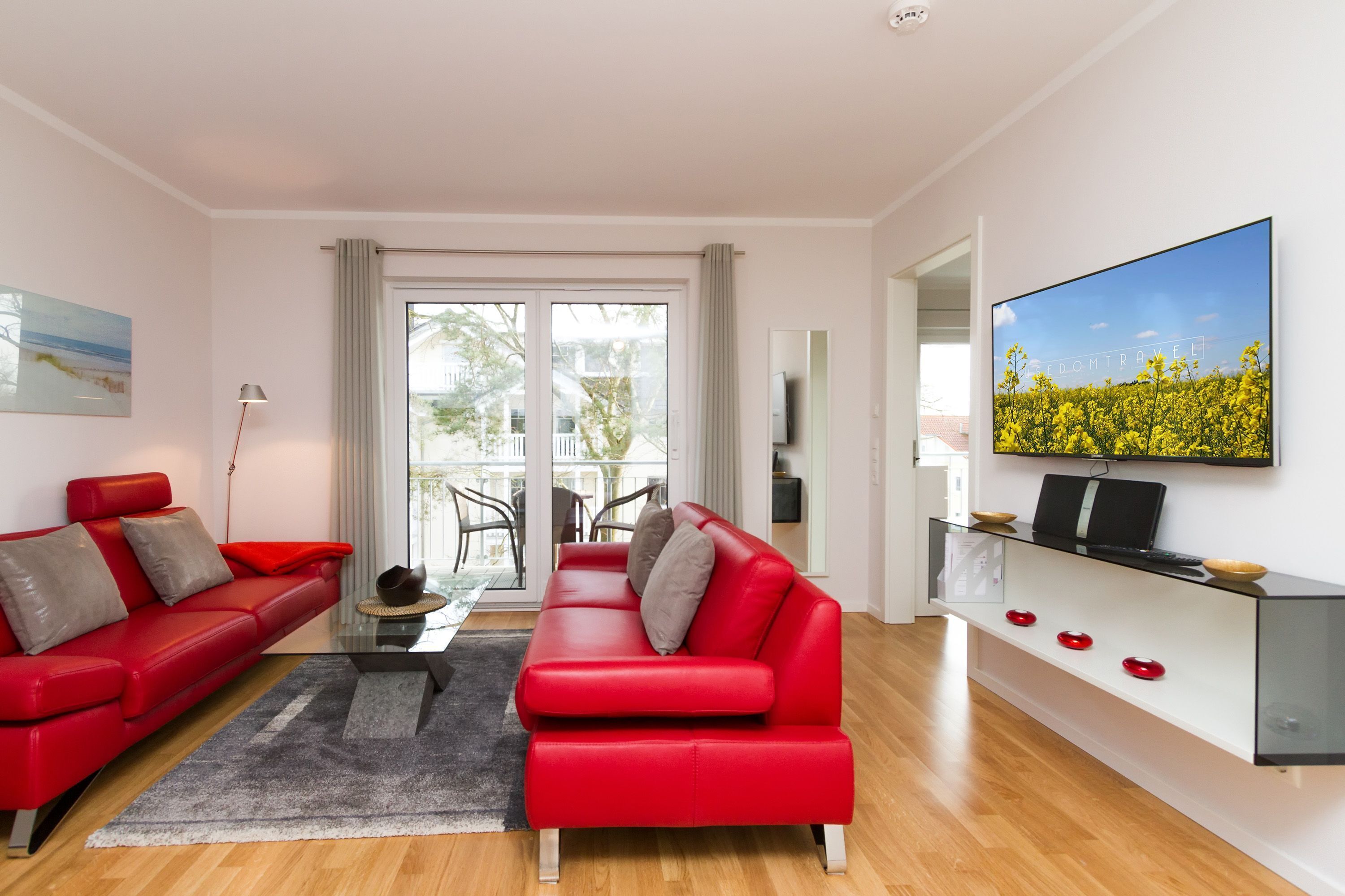 Ein modernes Wohnzimmer mit einem roten Sofa, einem Glastisch und einem flachbildfernseher an der Wand.