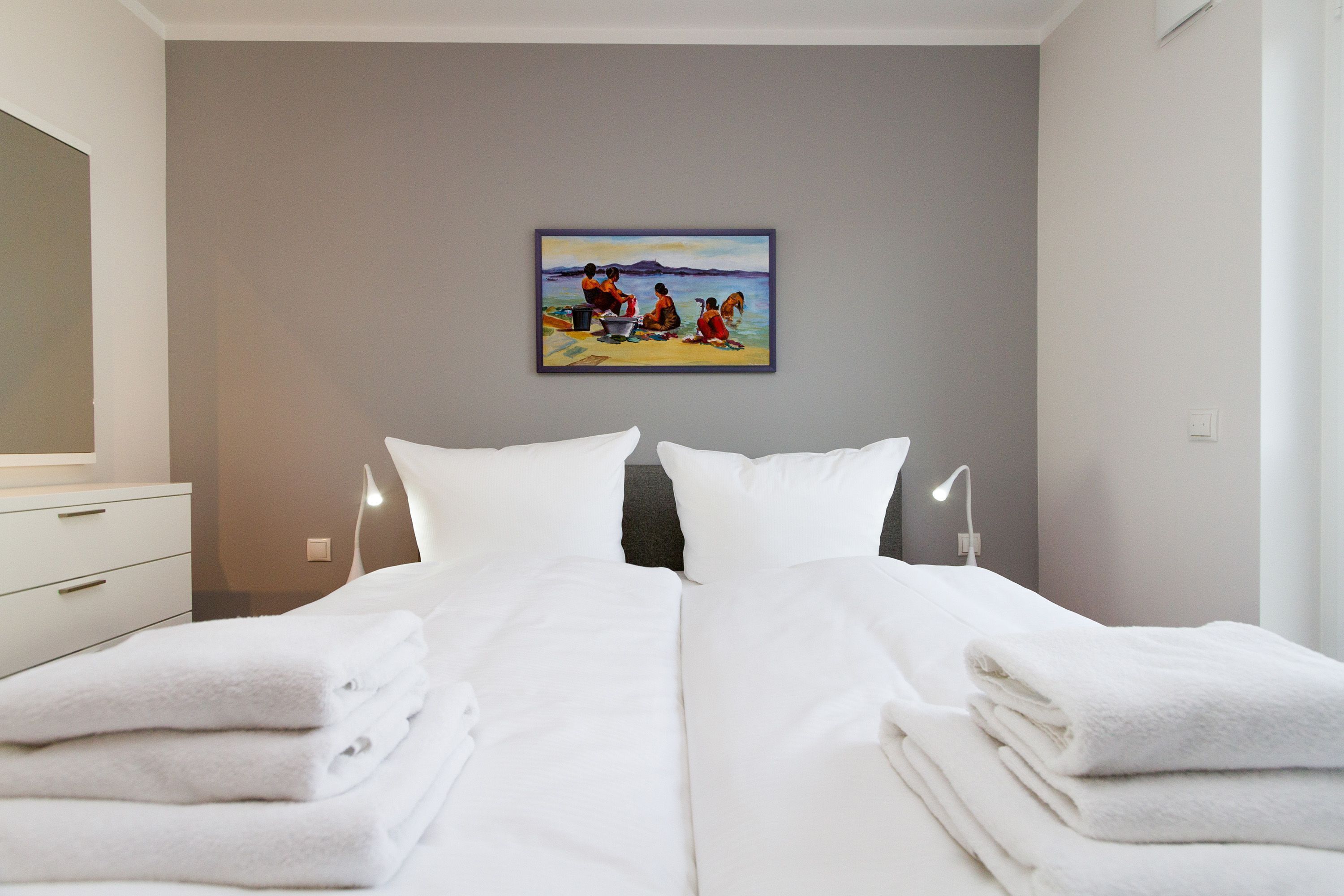 Habitación de hotel con cama, toallas blancas, un cuadro en la pared y una mesita de noche con lámpara.