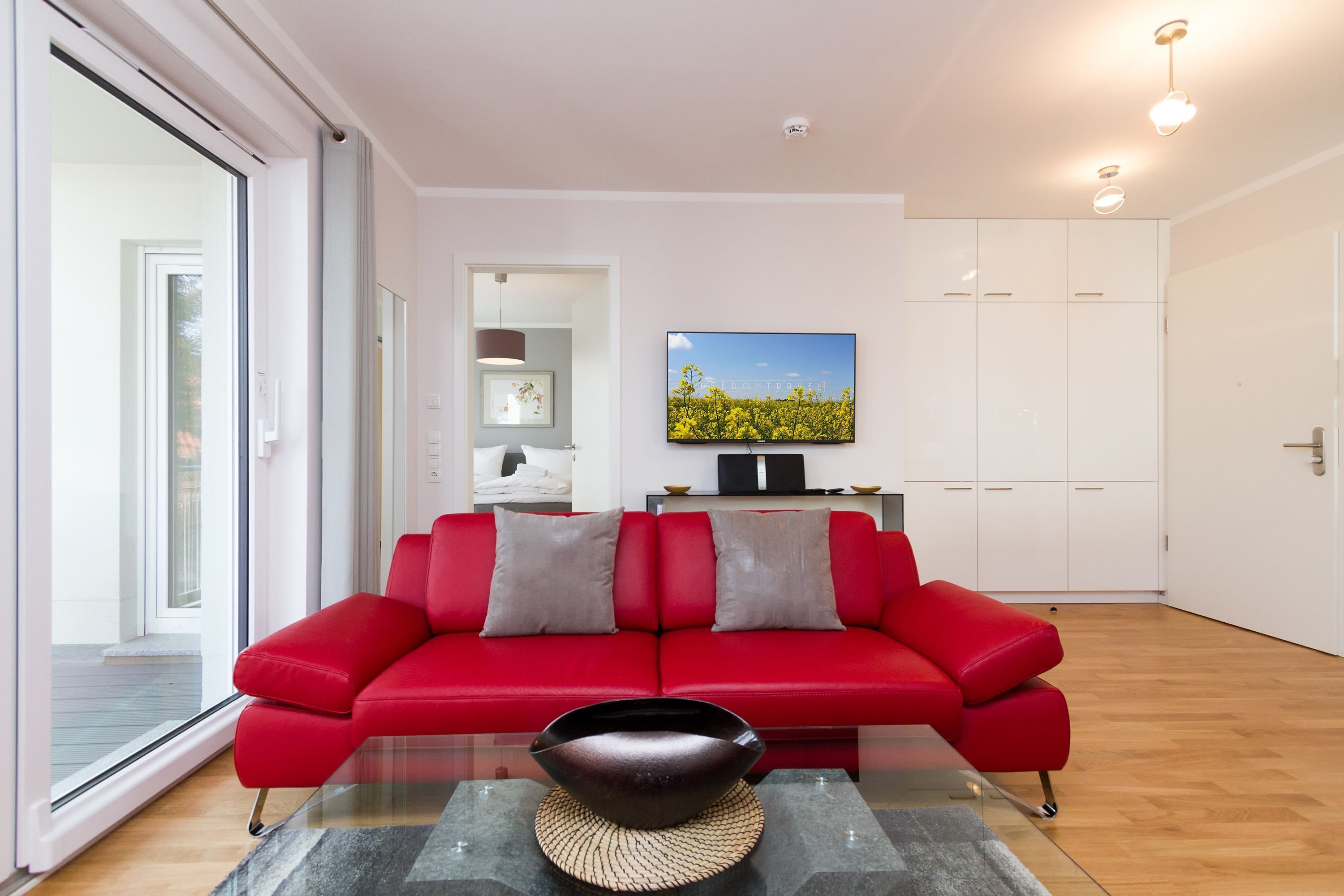 A modern living room with a red sofa, a flat-screen TV, and a large window.