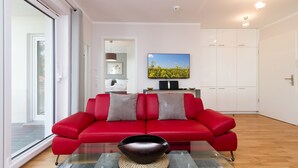 A modern living room with a red sofa, a flat-screen TV, and a large window. - Dune Residence Heringsdorf, App. 18 (Heringsdorf)
