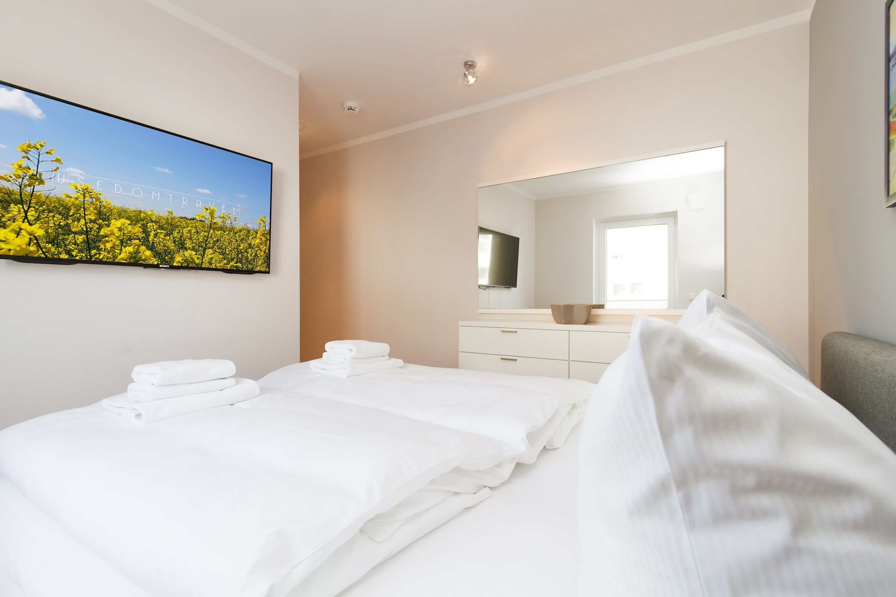 Ein Hotelzimmer mit einem großen Bett, einem Flachbildfernseher, einem Spiegel und einem Gemälde von einem Feld.