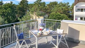Ein Balkon mit Frühstückstisch, umgeben von einer Brüstung und mit Blick auf eine Wohngegend mit Bäumen und Häusern.
