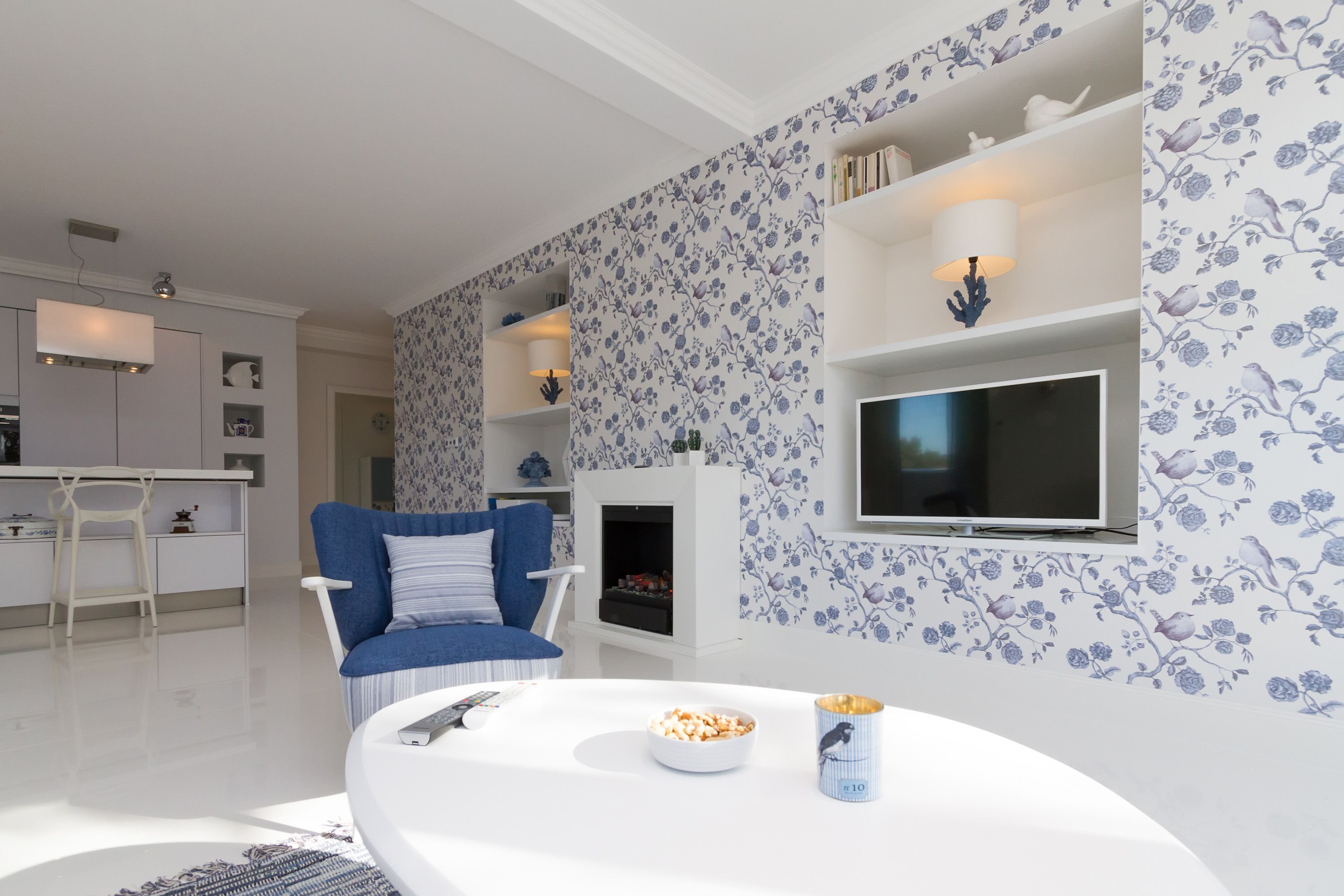 A modern living room with a blue sofa, a white coffee table, and a TV on the wall.