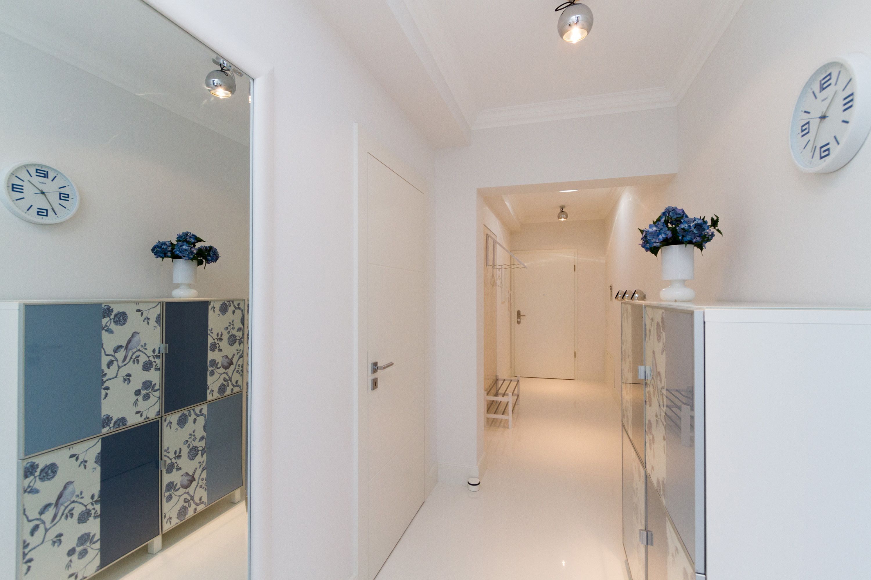 A hallway with a white door, a mirror, and a clock on the wall.