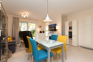 Une cuisine moderne avec un coin repas, comprenant une table et des chaises en verre, un luminaire suspendu et une vue sur l’extérieur.
