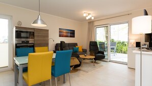 Ein modernes Wohnzimmer mit Essbereich, einer Sofagarnitur, einem Couchtisch und einer Küchenzeile mit Mikrowelle und Backofen.