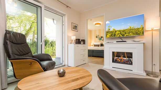 Ein modernes Wohnzimmer mit einer Couch, einem Couchtisch, einem Kamin, einem Fernseher und einer Glastür zum Balkon.
