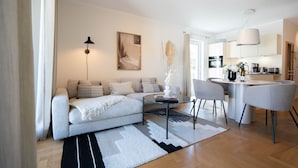 A modern living room with a sofa, a dining table, and a kitchen in the background. - Dünenresidenz Heringsdorf, App. 13 (Heringsdorf)