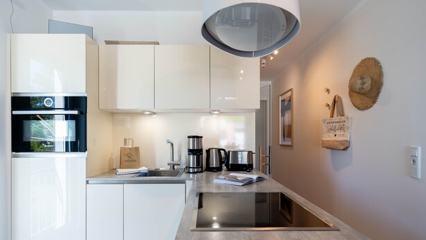 A modern kitchen with white cabinets, a built-in oven, a coffee maker, and a kettle. - Dünenresidenz Heringsdorf, App. 13 (Heringsdorf)