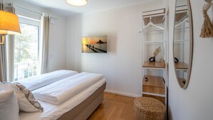 A bedroom with a bed, a hanging light, a painting, a wardrobe, and a mirror. - Dünenresidenz Heringsdorf, App. 13 (Heringsdorf)