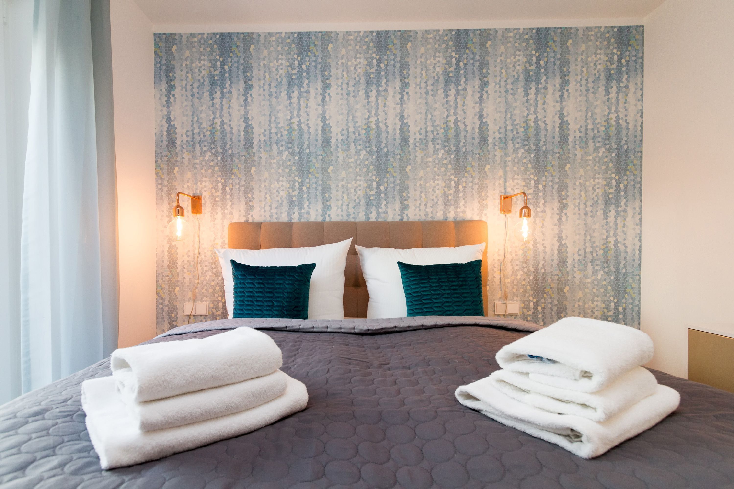 Une chambre d’hôtel avec un lit, deux lampes fixées au mur, une tête de lit et un mur à motifs.
