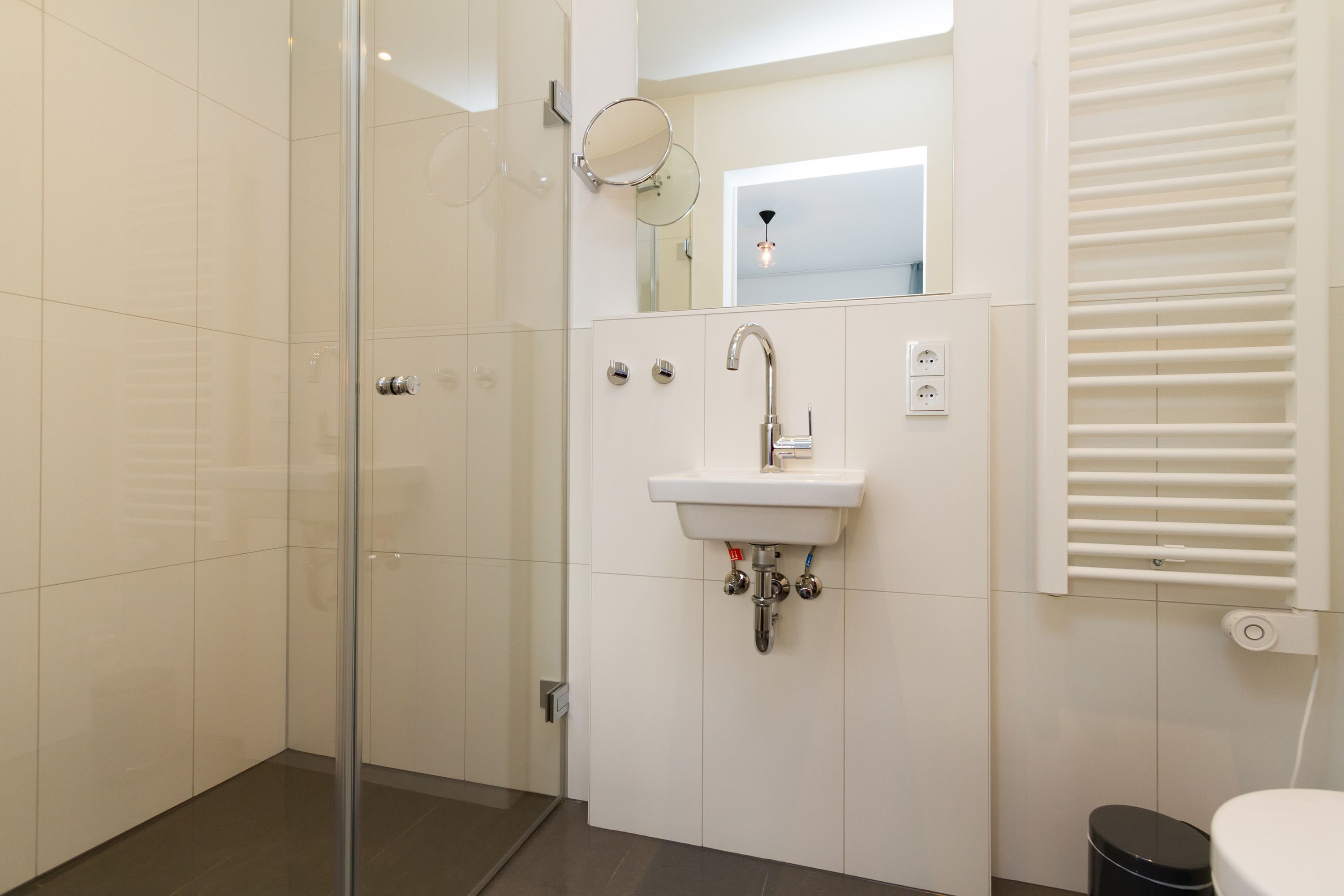 Une salle de bain moderne avec une douche à parois de verre, un lavabo blanc avec un miroir au-dessus, et des toilettes avec un abattant blanc.