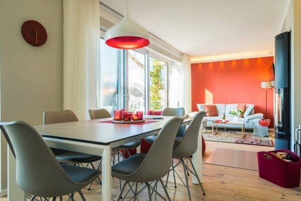 Un salon moderne avec un canapé blanc, des coussins rouges et un mur d’accent rouge.