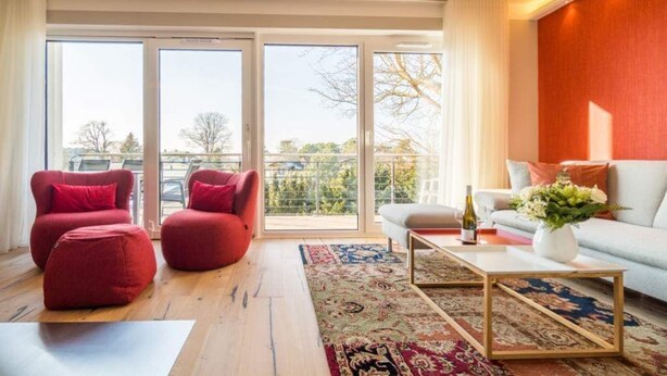 A modern living room with a sofa, red chairs, a coffee table, and a large window with a view of the outdoors. - Quartier am Fischerstrand, app. 4 (Heringsdorf)