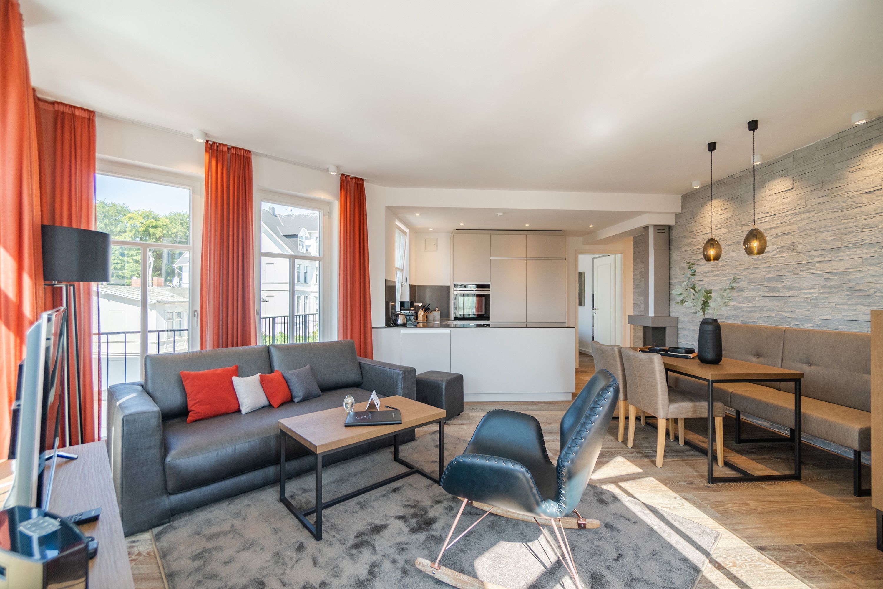 Un salon moderne avec un canapé, une table basse et des fauteuils, un coin repas avec une table et des chaises, et une cuisine en arrière-plan.