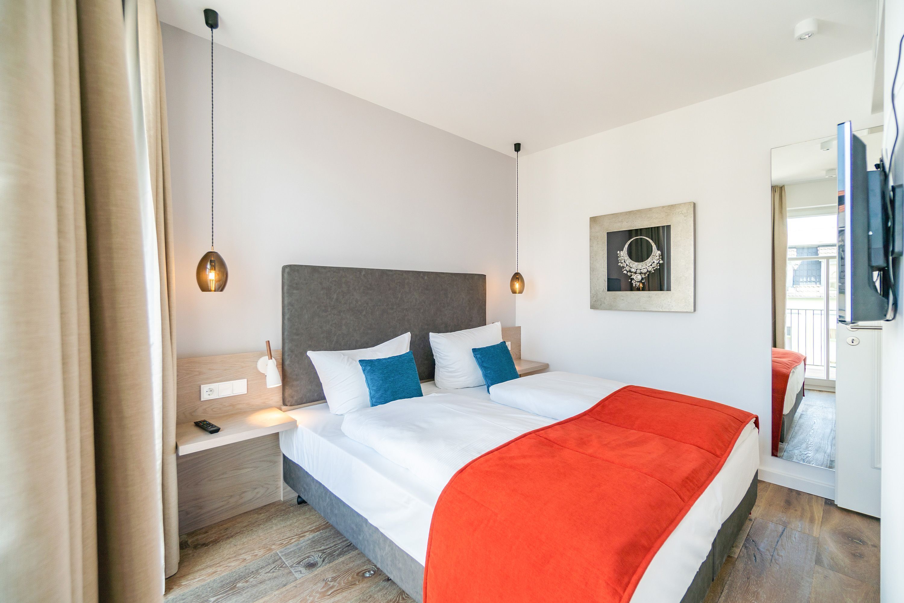 A modern hotel room with a large bed, a nightstand, a bedside table, a mirror, and a television.