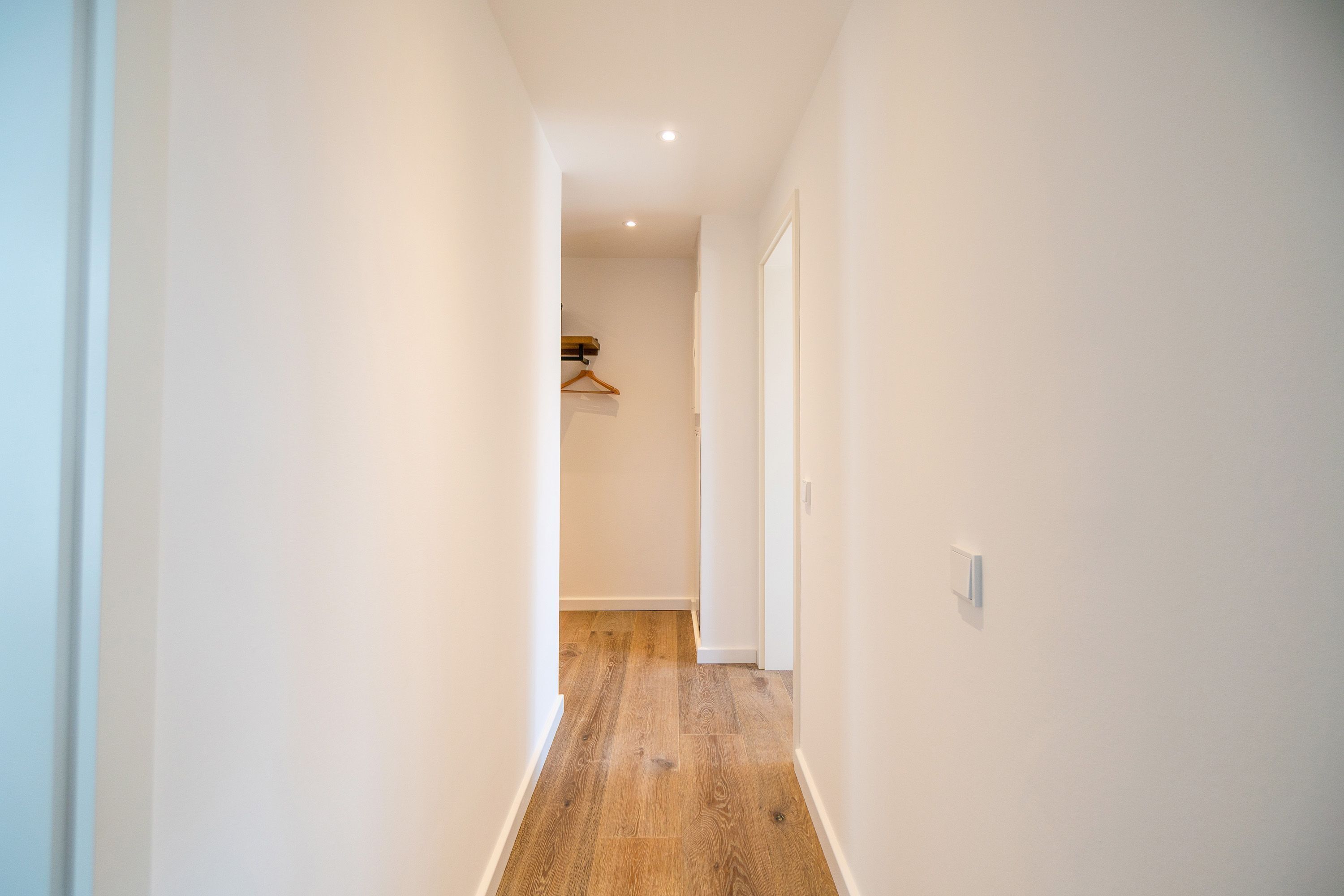 A narrow hallway with wooden flooring and white walls.
