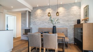 Eine moderne Küche mit Steinrückwand, Holzboden, einem Essbereich mit Tisch und Stühlen sowie Pendelleuchten.