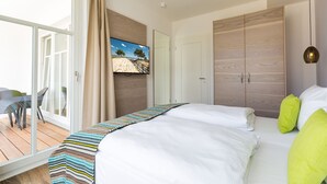 A bedroom with a large bed, a wooden wardrobe, a television on the wall, and a balcony with a table and chairs. - Beachhouse Bansin, App. 16 (Heringsdorf)