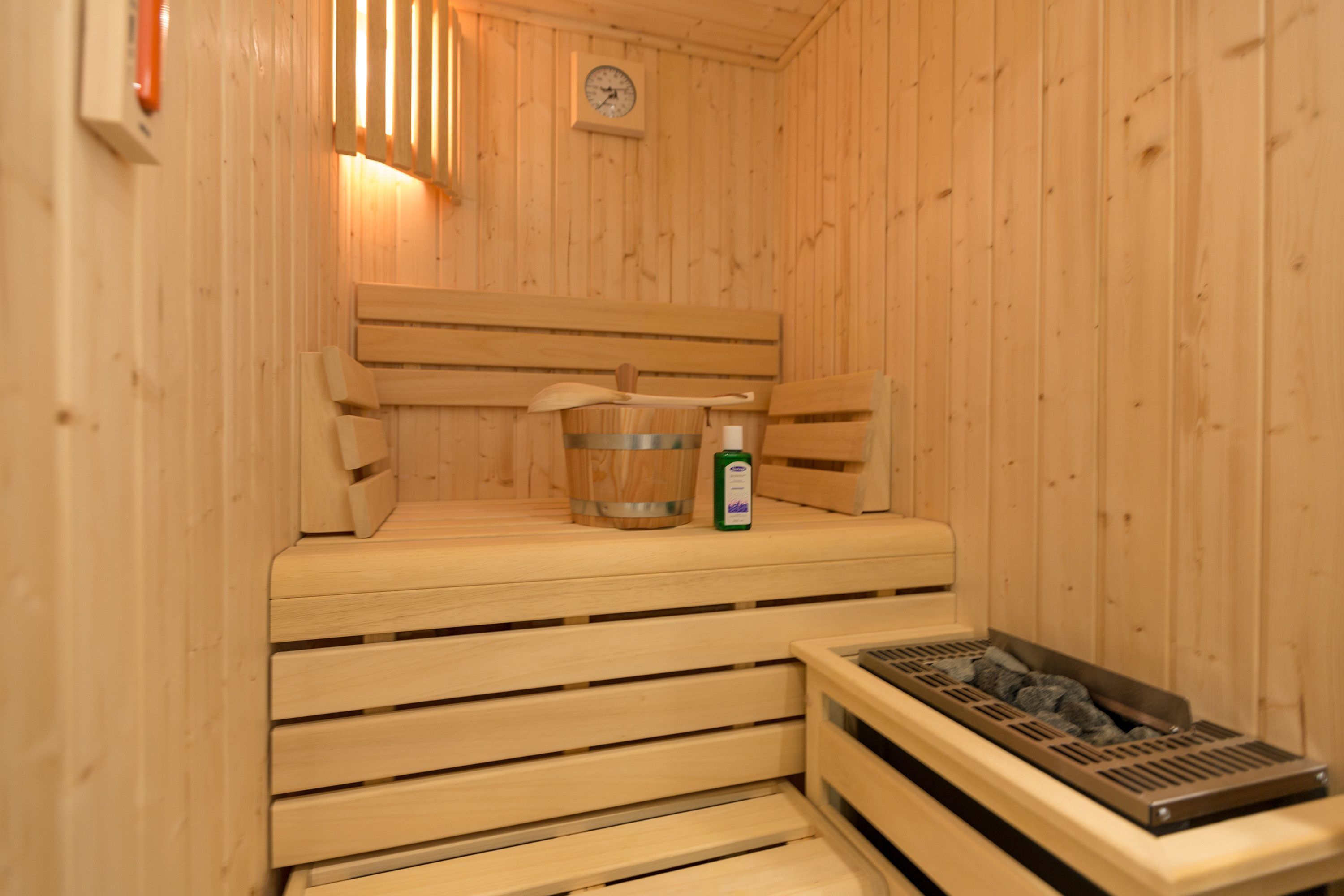 A sauna with wooden benches, a wooden wall clock, and a metal container with a wooden spoon.