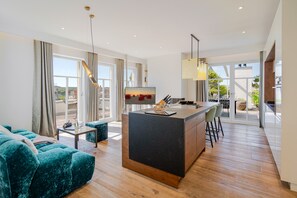 A modern living room with a sofa, a coffee table, a kitchen island with bar stools, and large windows. - Beachhouse Bansin, Penthouse Sunset (Heringsdorf)