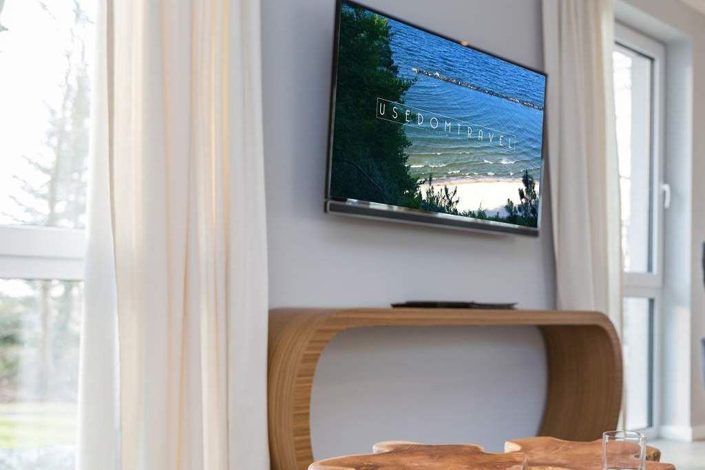 Ein modernes Zimmer mit an der Wand befestigtem Fernseher, einem Holzstuhl und einem Glastisch.